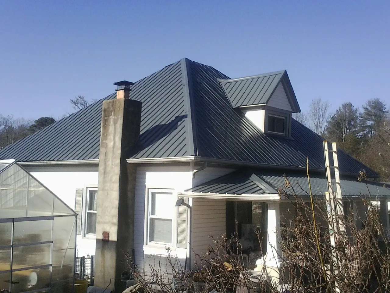 Dark blue standing seam metal roof on a white farmhouse with dormer — Slate & Tile Roof Repair by Roofing Brothers in Sun City Center