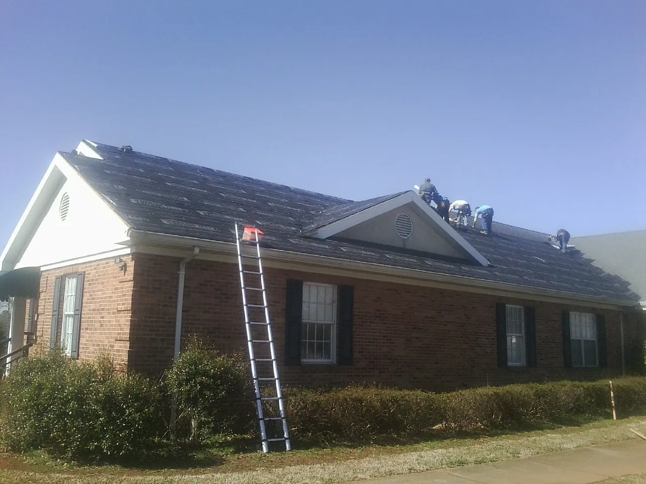 Crew tearing shingles off a brick ranch roof with a ladder set — Metal Roof Repair work by our crew in Sun City Center