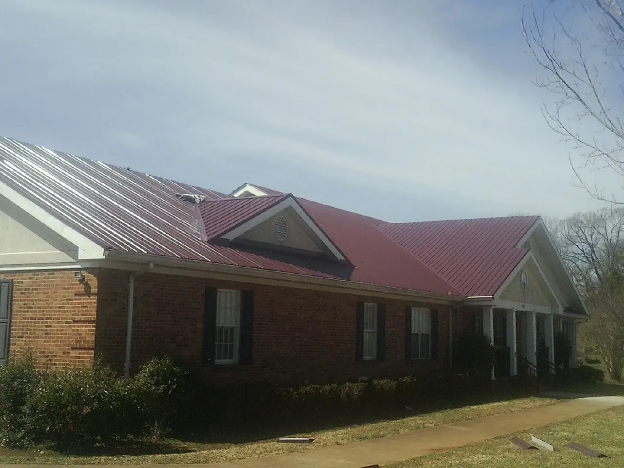 Red metal roof with gabled entries on a long brick building, from a Hail Damage Roof Repair job in Sun City Center