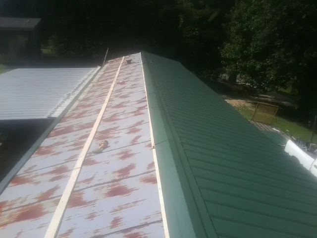Old rusted panels beside newly installed green metal roofing — Wind Damage Roof Repair by Roofing Brothers in Sun City Center