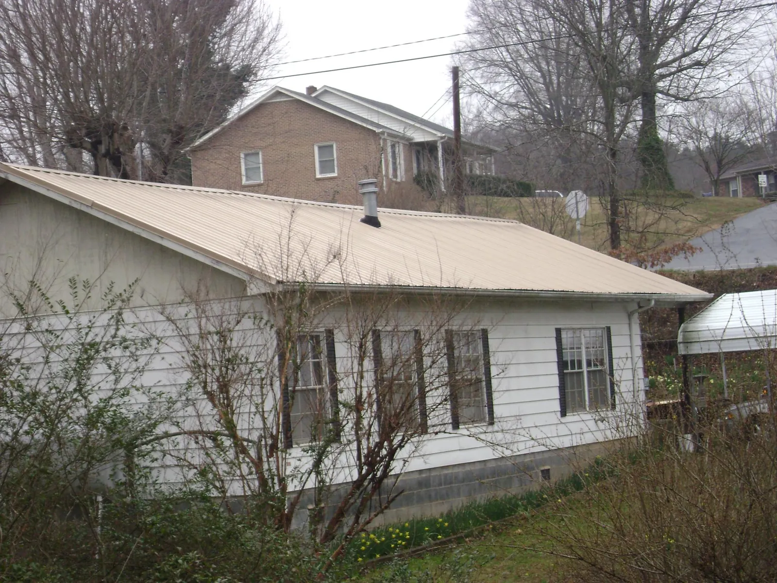 Tan metal roof on a white sided house set into a hillside — Commercial Roofing by Roofing Brothers in Sun City Center